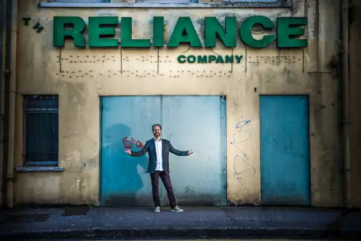Oliver Moran standing outside a building with the words Reliance Company in large green lettering.